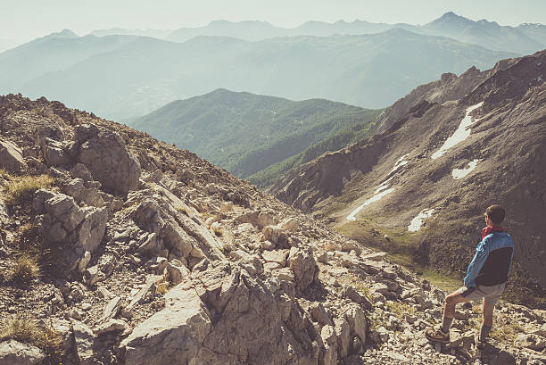 Hiker standing on steep rocky mountain footpath and looking at the wide panorama. Concept of reaching the goal and conquering the success. Toned image, vintage style, desaturated.