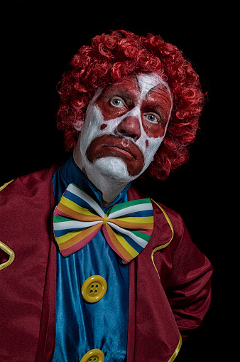 Clown in a yellow costume standing in front of a mirror isolated on white background
