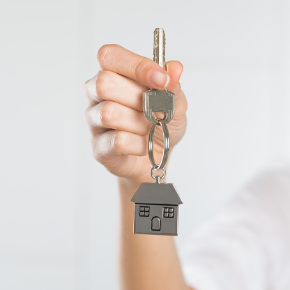 Closeup shot of a woman holding key of her new house. Woman buying new home and showing key. Shallow depth of field with focus on house key.