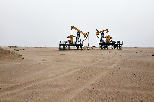 Oil pump in the desert sand on the shore of the Sea of Okhotsk. Gray cloudy sky background