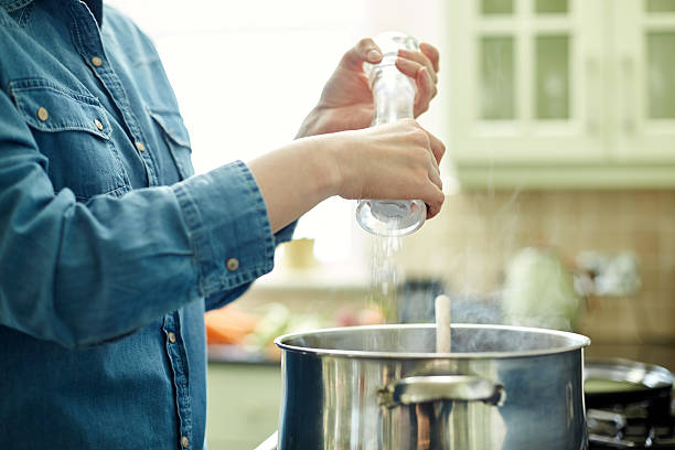 woman 塩をふるからシェーカーにキッチンで調理する鍋 - 塩をふる ストックフォトと画像