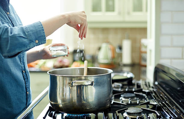 Woman adding salt to cooking pot on stove Midsection image of woman adding salt in cooking pot. Utensil is placed on gas stove. Close-up of female seasoning her dish. She is preparing food in domestic kitchen. salt seasoning stock pictures, royalty-free photos & images