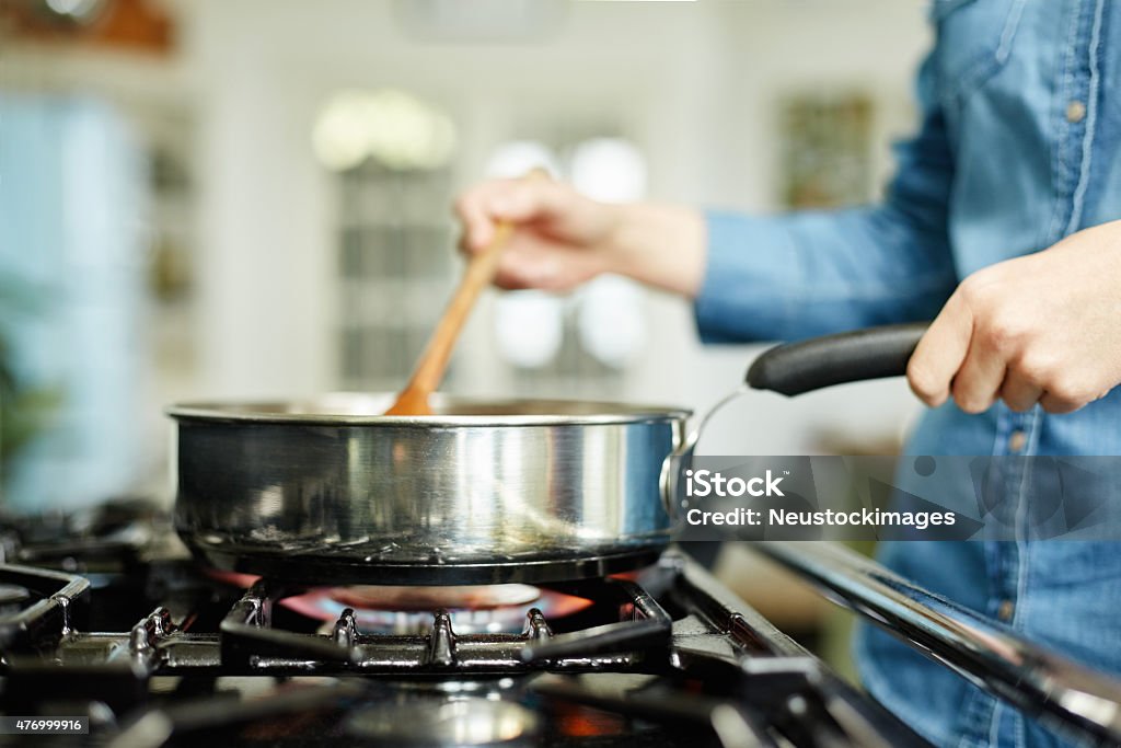 Close-up of woman cooking food in frying pan Close-up midsection image of woman cooking food in frying pan. Utensil is placed on gas stove. Female is stirring food in cooking pan. She is preparing food in domestic kitchen. Gas Stove Burner Stock Photo