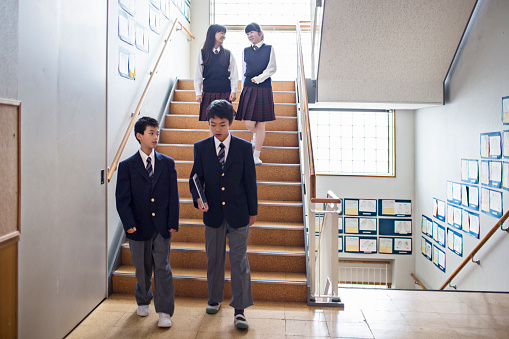 Japanese students walking in the school staircase, two boys in the front and two girl in the back talking.