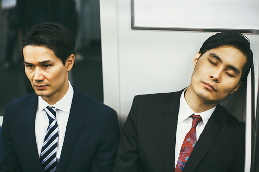 Two handsome asian businessmen in subway. One of them is sleeping. Concept for modern business and lifestyle. Image is taken during Tokyo istockalypse 2015.