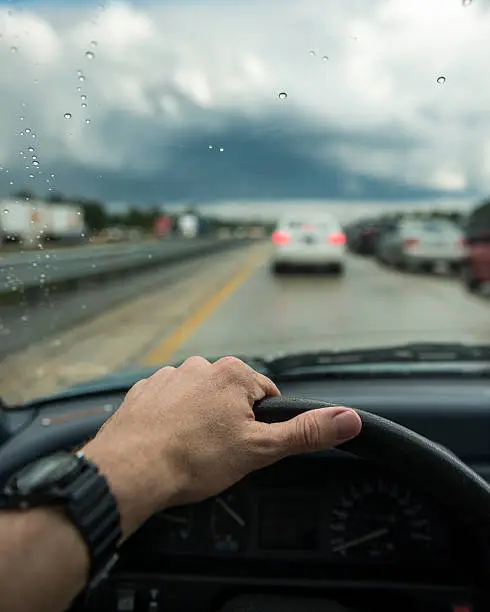A driver's hand rests on the steering wheel while stuck in traffic as a thunderstorm moves through the area. Jacksonville, Florida.