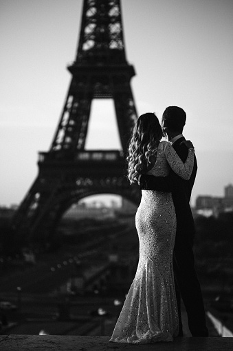 Black and white photo of young married couple hugging in Paris. There is an Eiffel tower in the background.