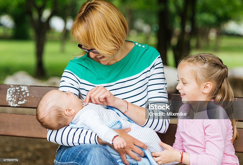 Family in the park Young mother playing with her kids in the park. She is holding her baby boy and on the right is her daughter. Casual clothing. Mother Stock Photo