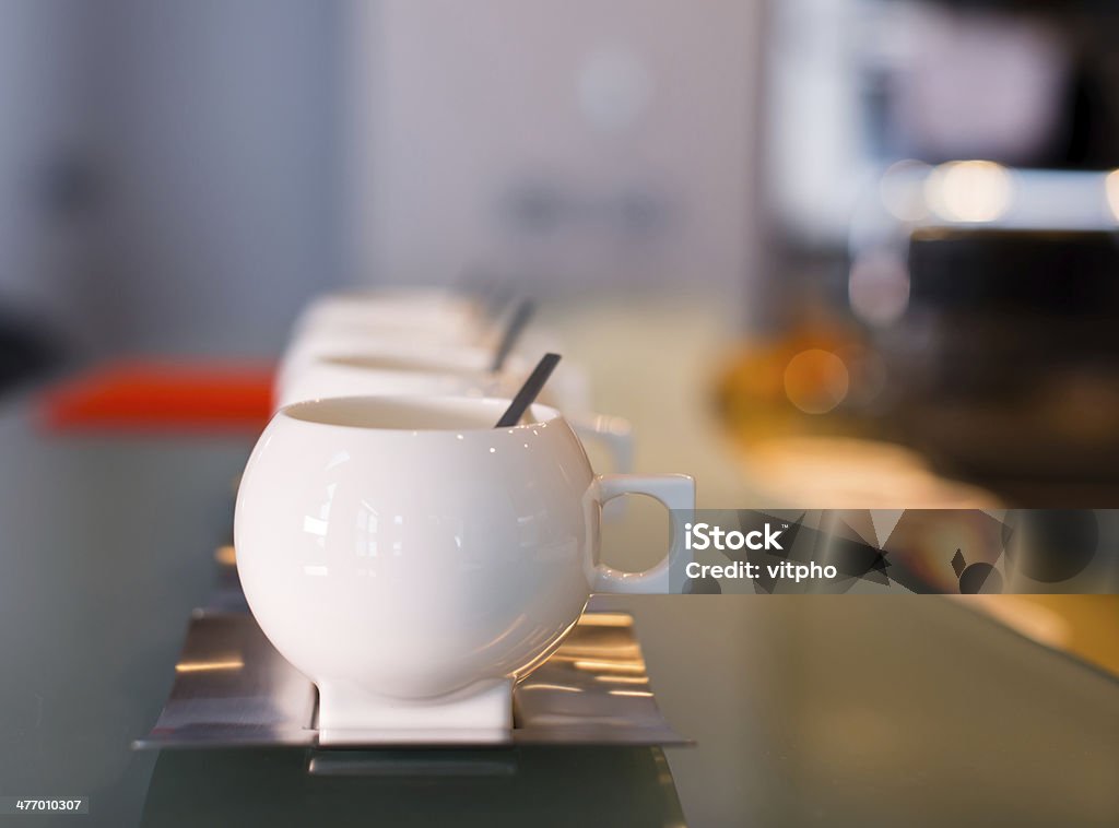 White porcelain contemporary cups with stainless steel saucers and spoons White porcelain contemporary cups with stainless steel saucers and spoons on glass counter top and blurred background with light spots Afternoon Tea Stock Photo