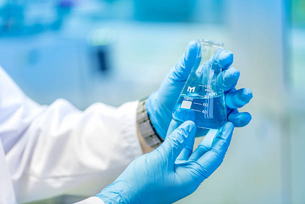 arzt hält reagenzglas, glaskolben mit blau flüssig in labor - technitian stock-fotos und bilder
