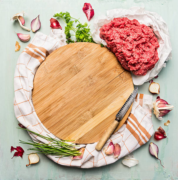 Minced meat with herbs and spices around wooden cutting board