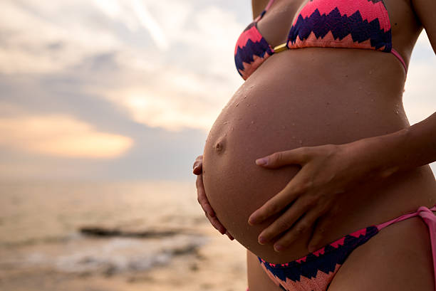 schwangere frau am strand hält ihr bauch - third generation stock-fotos und bilder