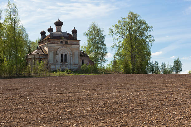 Plowed field on a background of crumbling church Plowed field on a background of crumbling church. Concept of rebirth of life. Church of the Nativity of the Blessed Virgin in a village Zhavoronkova Verhovazhskogo district Vologda region Russia fracturable stock pictures, royalty-free photos & images