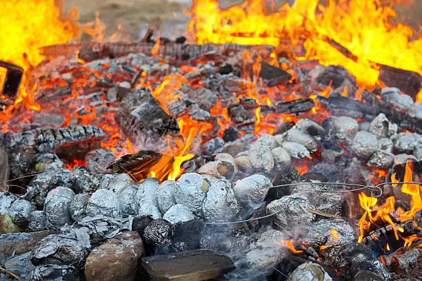 Baked potatoes covered with aluminum foil roasting in a Lag Baomer bonfire with orange flames and firewood in a secular suburb of Tel Aviv, Israel