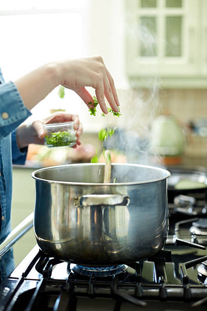 istock Woman adding cilantro to cooking pan on stove 477022368