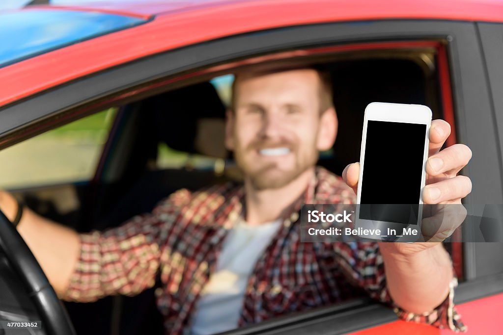 Man in car driving showing smart phone Man in car driving showing smart phone display smiling happy. Focus on smartphone. 2015 Stock Photo