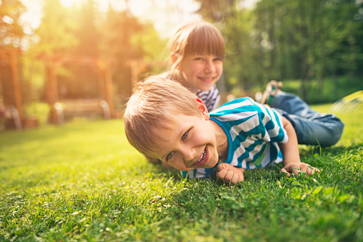 Little boy aged 5 and his elder sister aged 9 are having fun laughing on the garden lawn grass.