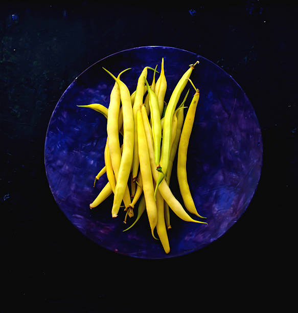 tas de grains de jaune ciré sur blue plate - wax bean photos et images de collection