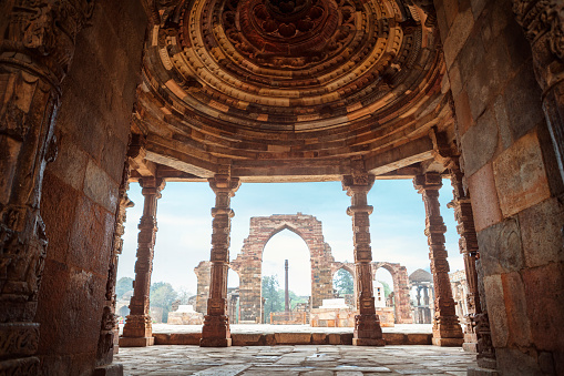 The Iron Pillar through the cloister columns at Quwwat ul-Islam Mosque in ruins of Qutb Minar Complex in New Delhi, India.