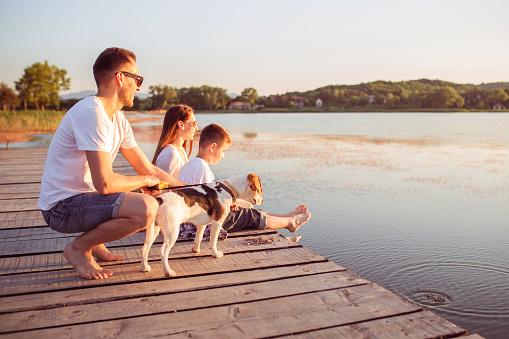 Family of three member plays with dog sitting on the dock by the lake and enjoy the outdoors.