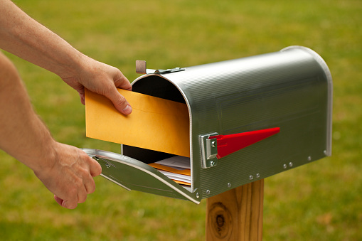 Hand reaching into a mailbox to send a letter.