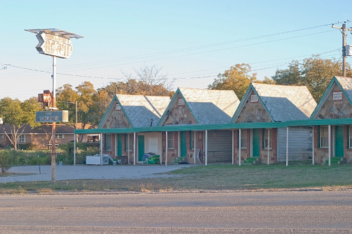 A 1930s vintage roadside motor court motel has a sign.  Each of the 4 units has a peaked roofline, a stone facade, and bright green trim and door.  Taken in the very late afternoon sun in early fall.