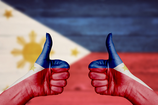 Philippines flag painted on female hands thumbs up with blurry wooden background