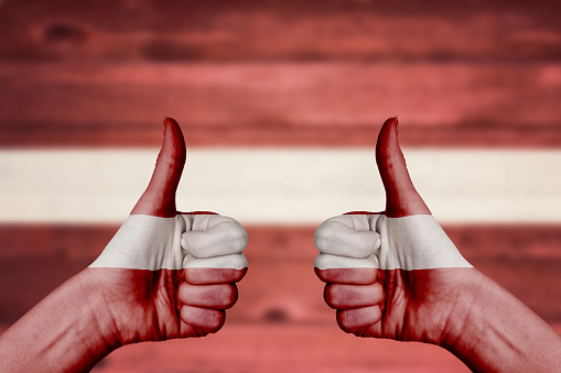 Lativa flag painted on female hands thumbs up with blurry wooden background