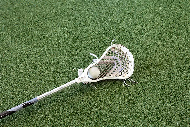 A lacrosse stick and ball lay on turf.