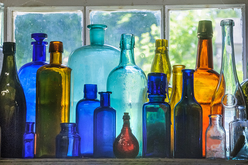 A collection of antique glass bottles in a dusty shop window in the Hudson River Valley of New York.