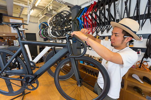 Japanese small businessman working in a bike shop surrounded by different brands of bicycles and bike parts