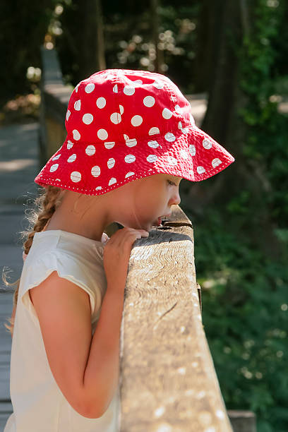 Girl in red white polka dots panama looks down from a bridge against green foliage background was taken.