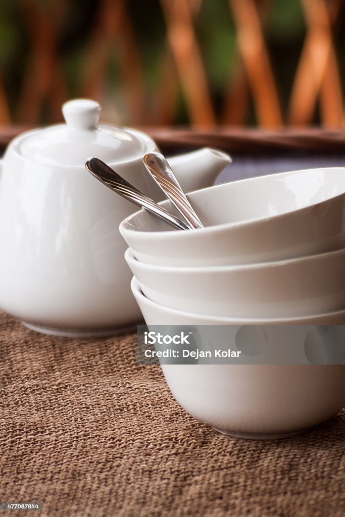 Stack of bowls and a tea pot. Stack of white clay bowls with spoons inside and white tea pot on burlap 2015 Stock Photo