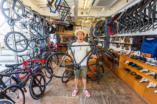 Japanese small businessman holding a bicycle in a bike shop surrounded by different brands of bicycles and bike parts
