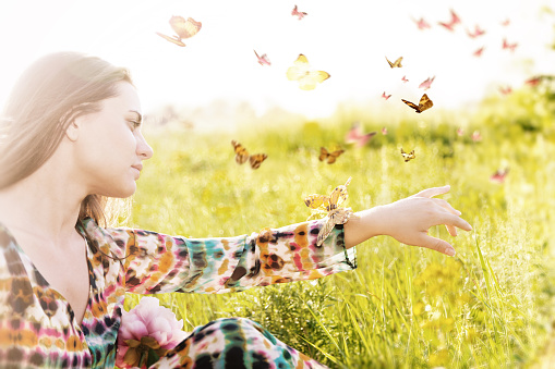 Summer mood. Girl sitting in a meadow in a swarm of flitting butterflies.