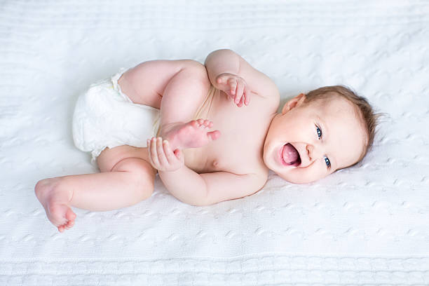 lustiger laughing baby tragen eine windel spielen mit ihren füßen - nur babys fotos stock-fotos und bilder