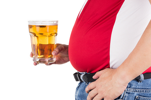 Obese man with big belly holding a glass of refreshing cold beer