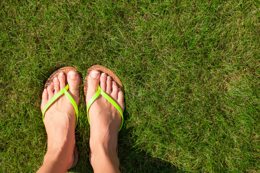 Low section of woman wearing jeans with barefoot walking on grassy field at park