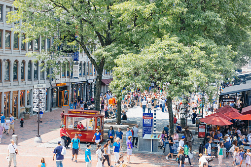 Faneuil Hall Marketplace in Boston, Massachusetts USA, which is a cobblestone promenade where there are lots of shops. People are also visible in the image.