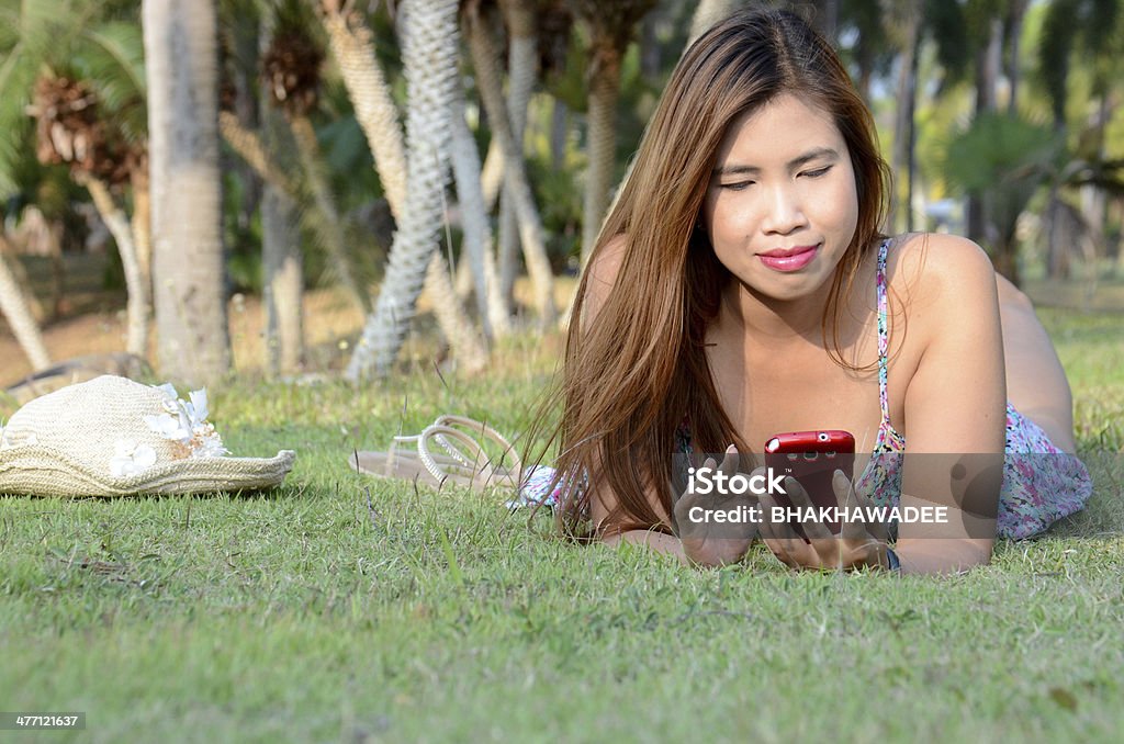 Woman lay on the grass Woman lay on the grass and enjoy to playing her mobile phone Adult Stock Photo