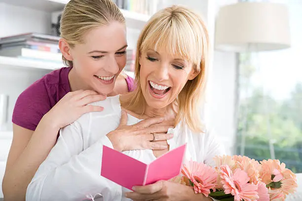 A daughter giving her mother flowers with a card.