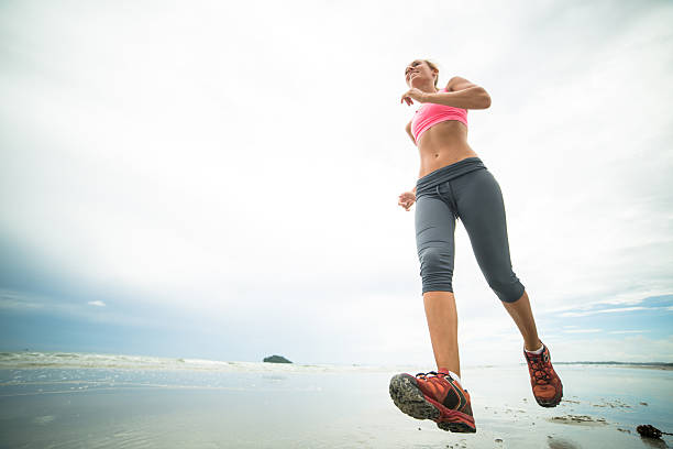 Young woman jogging on the beach on a cloudy day. Low angle view.