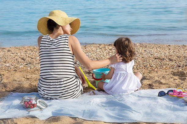 istock Mother stroking daughter on beach 477128890