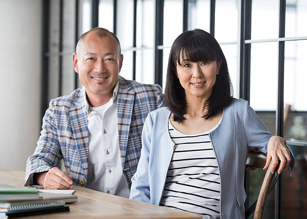 Japanese couple sitting at table Modern Japanese couple sitting at table. Portrait of mid adult Asian woman and mature man at home. mid adult couple stock pictures, royalty-free photos & images