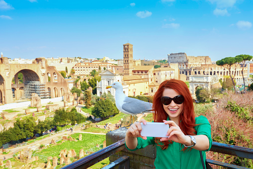 attractive red hair woman in Rome making herself a picture with her mobile phone, Rome city scape in background.