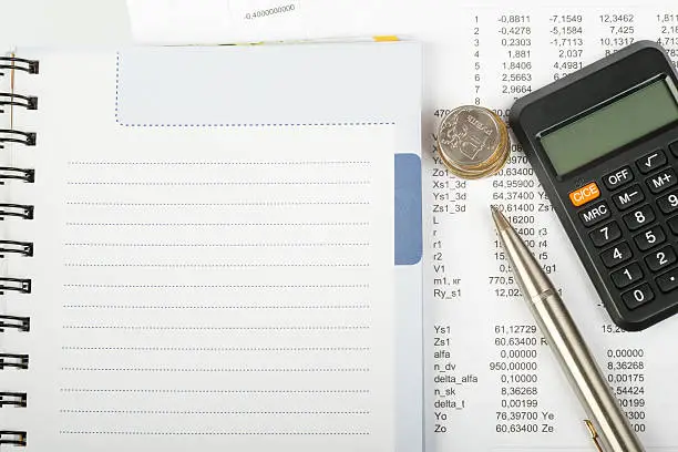 White ring-bound notebook with coins and calculator, close-up view