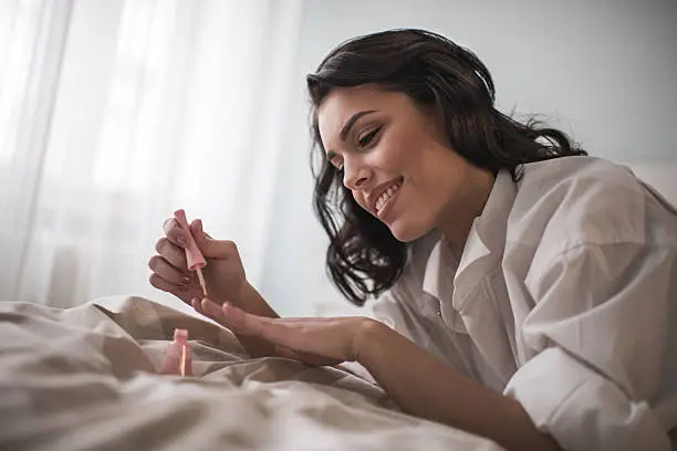 Photo of Young smiling woman having manicure treatment in bedroom.