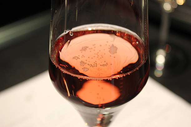 Glass of Sparking Wine on a Blurred White Counter The image is set to show a bar, restaurant or cafe setting, with a glass of sparkling rose wine (champagne) against a blurred white counterspace, with hints of stainless steel as well. The dominant colors are light red, copper, pinkish red, white and some grays.  rose champagne stock pictures, royalty-free photos & images