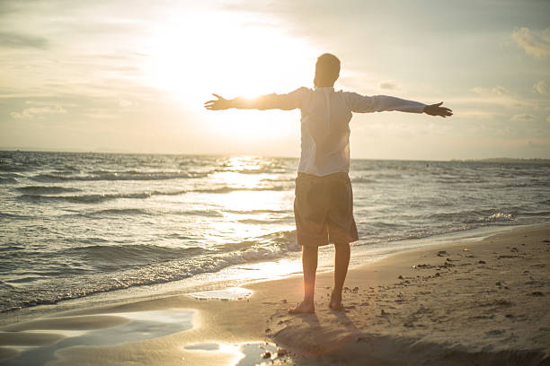 istock Man on the beach opens arms to sunset 477158566