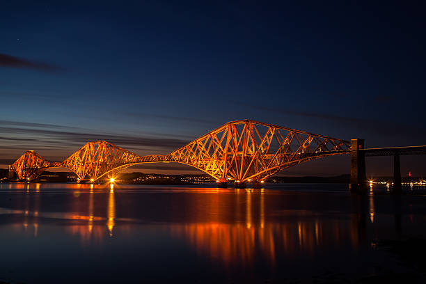 Forth Rail Bridge over the Firth of Forth in Scotland; Lights eliminate the bridge against the night sky. Lights are reflected on the water